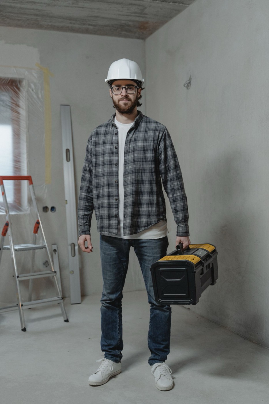 Ampcrest electrician in a hard hat and plaid shirt with his toolbox inside a home under renovation