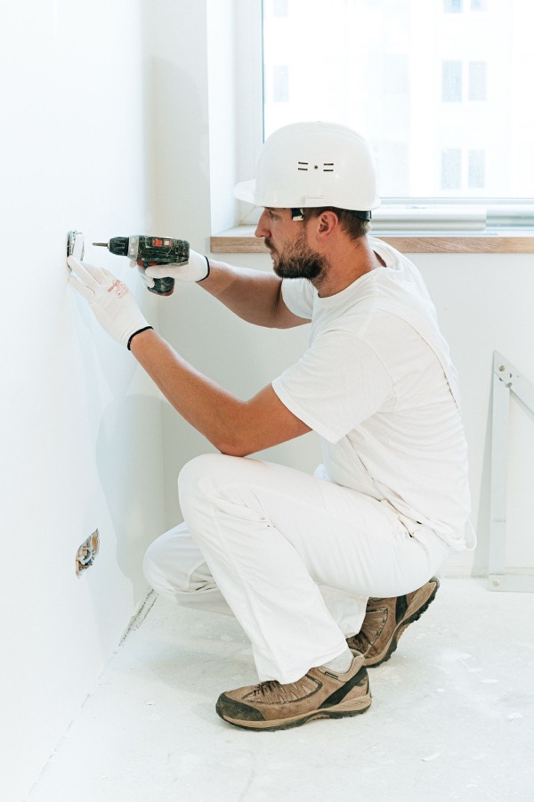 Electrician in a hard hat testing a wall outlet